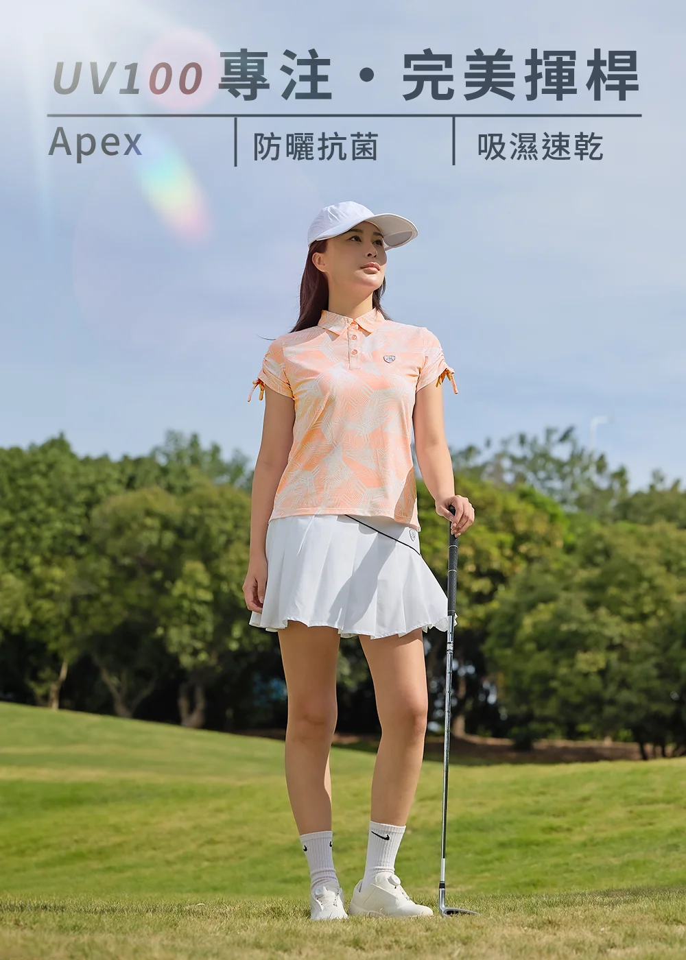 UV100 Apex 女士高爾夫防曬 Polo 衫穿搭:女模特兒戴白色遮陽帽,身穿粉橘色幾何印花短袖 Polo 衫與白色防曬百褶短裙,手扶高爾夫球桿,展現『專注·完美揮桿』的吸濕速乾高球休閒風格。