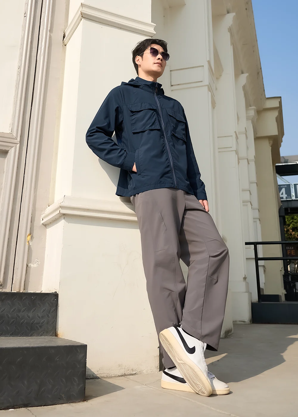 戶外機能服飾穿搭推薦:深藍色連帽防曬外套搭配灰色修身長褲與運動鞋,展示適合旅行與日常活動的輕量化裝備。