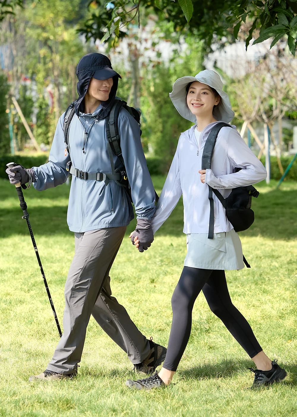 男女模特兒穿著 Suptex 防曬機能外套與登山裝備,於綠地步道健行,展現夏季戶外運動的情侶穿搭風格