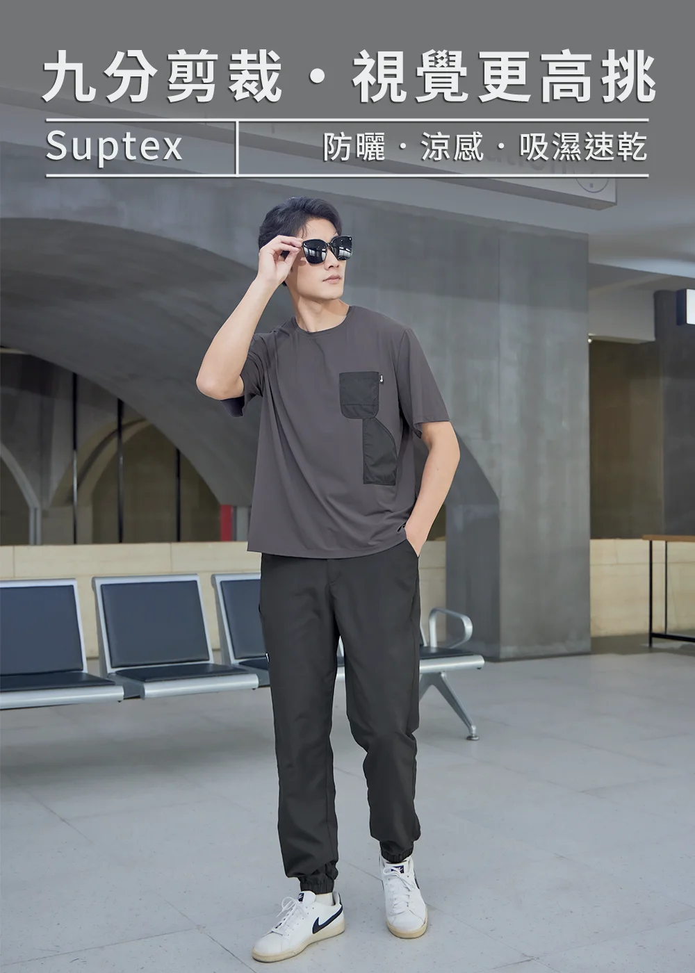 男模特兒身穿深灰色Suptex涼感防曬機能短袖T恤與九分剪裁黑長褲,配戴墨鏡站立於車站大廳,展現吸濕速乾與視覺更高挑的城市休閒穿搭