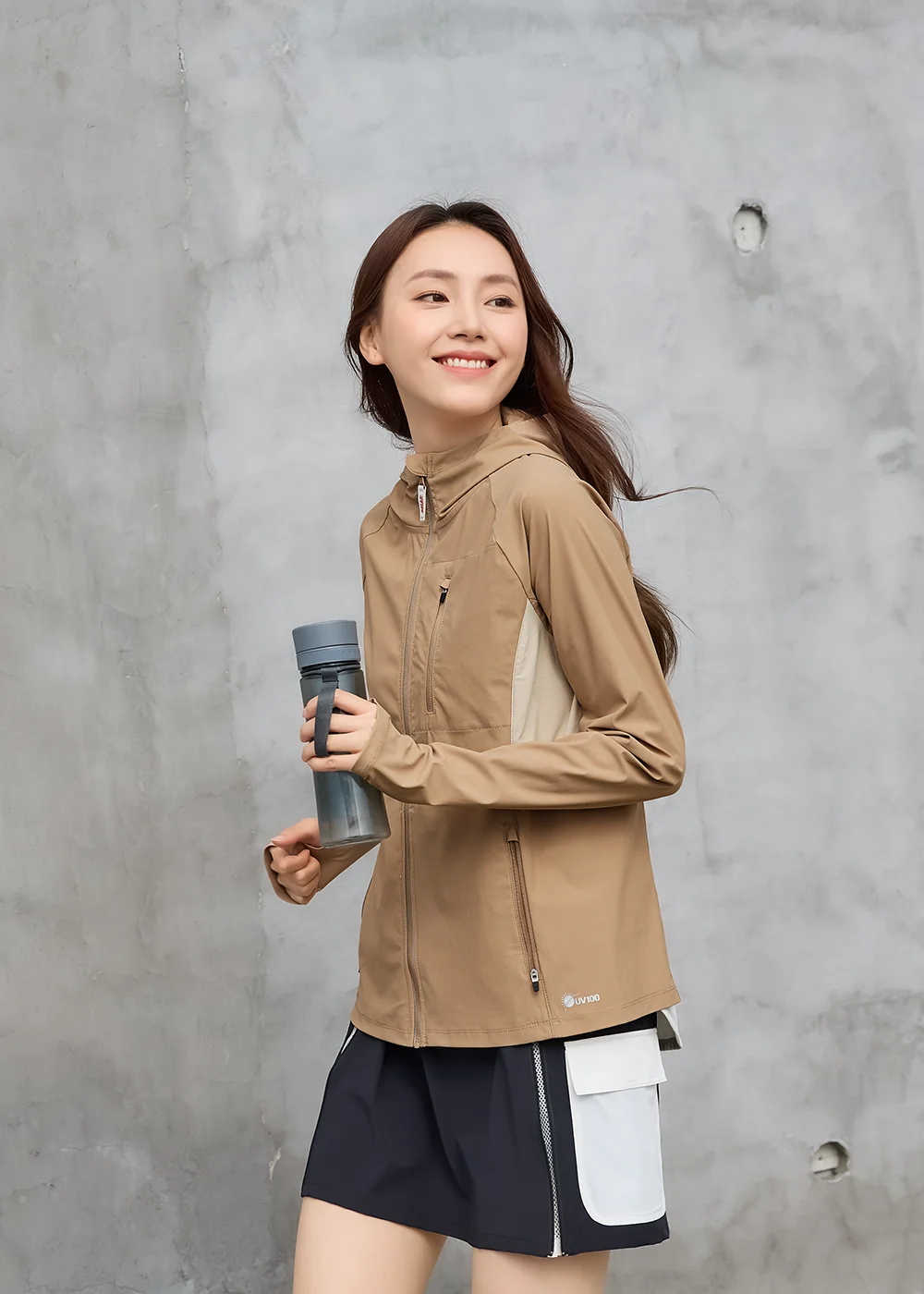 女模特兒穿著卡其色防曬外套,手拿灰色運動水壺正在跑步,展現外套在運動時的律動感與排汗透氣機能。
