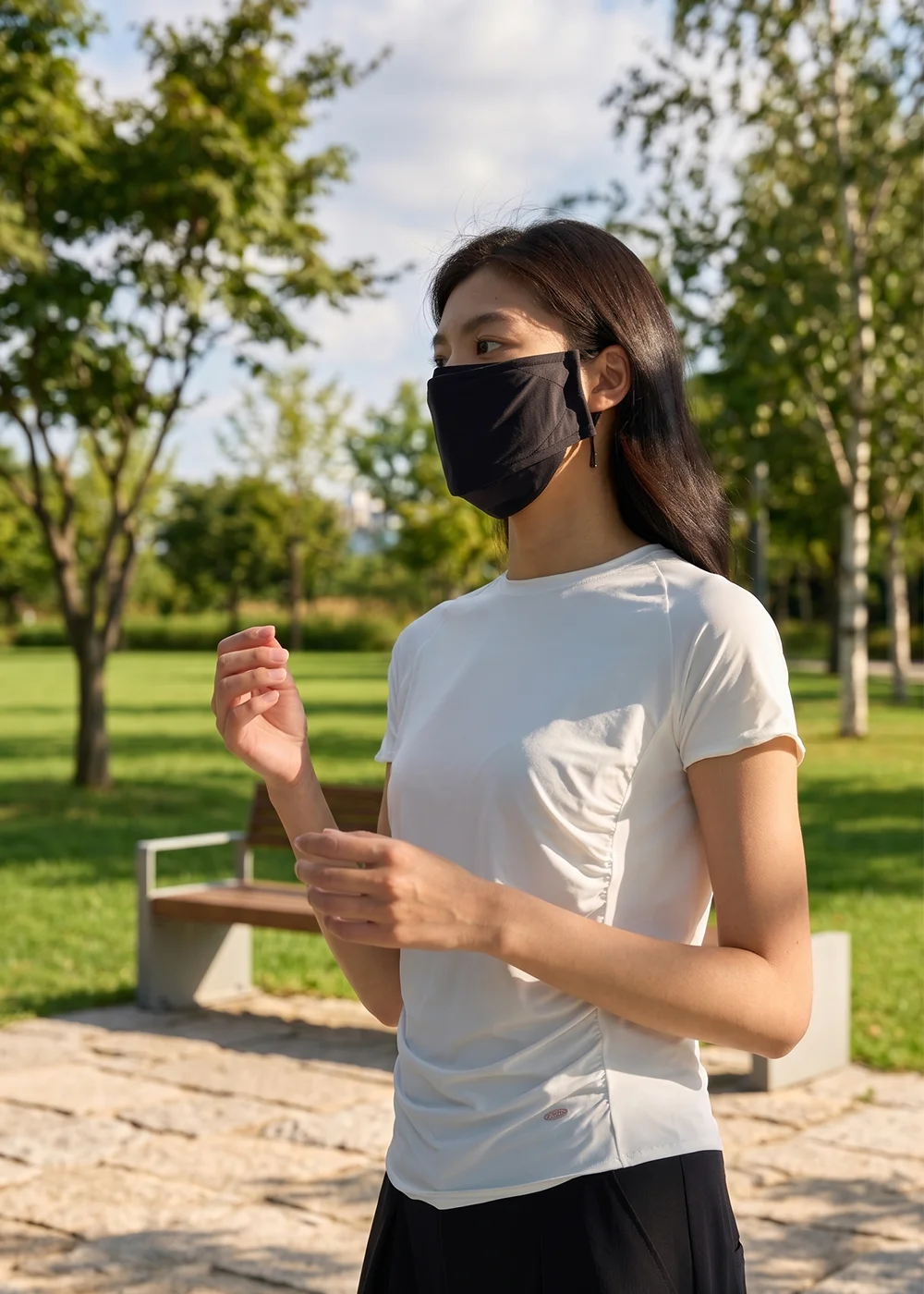 UV100 美型立體抗紫外線口罩:女模特兒身穿白色運動休閒短袖、黑色運動下著,配戴黑色加大版機能防曬口罩,在綠意樹林與石磚步道情境下呈現通勤防曬穿搭。