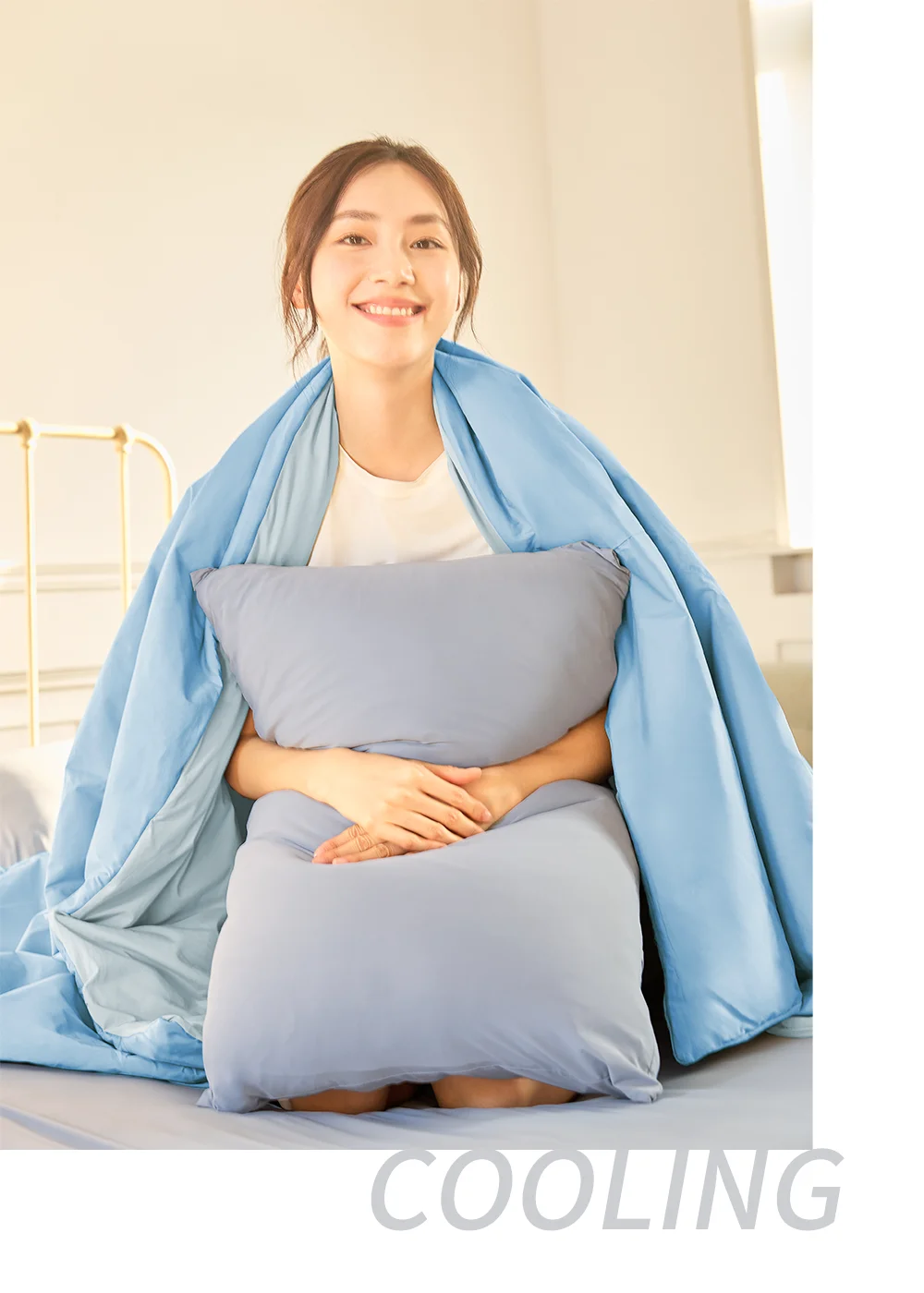 女模特兒坐在床上環抱枕頭並披著 抗UV-Apex涼感彈性雙面被,突顯其高密棉平織布料在室內自然採光下的細緻垂墜感與輕盈柔軟舒適度。
