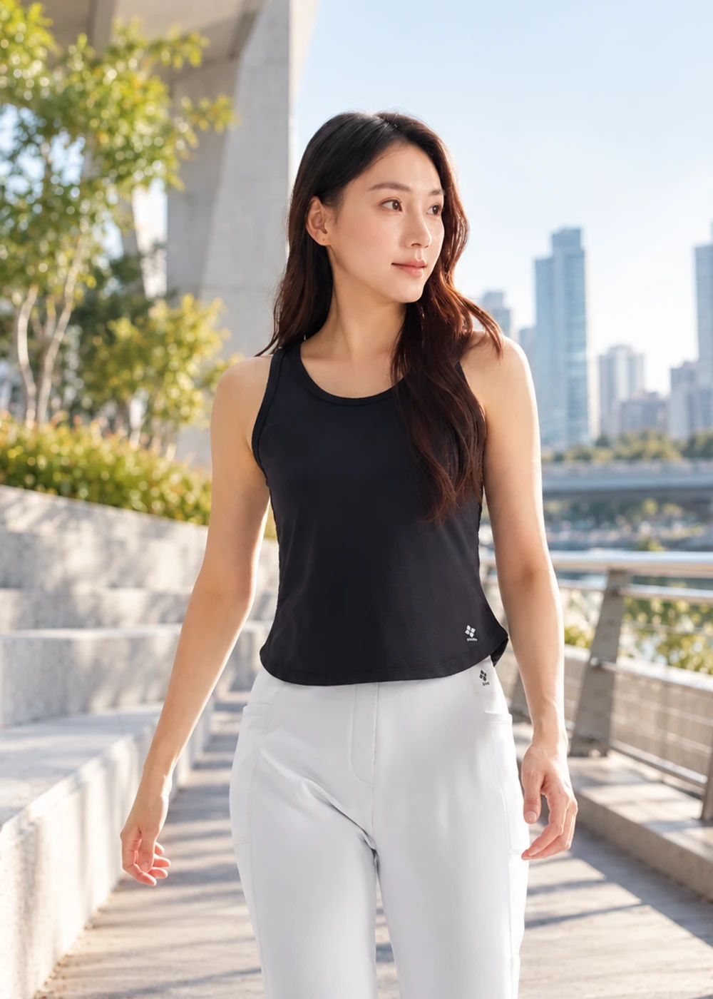 女性模特兒在戶外漫步,身穿黑色科技羊毛背心與淺灰長褲,展示合身剪裁與側身輪廓