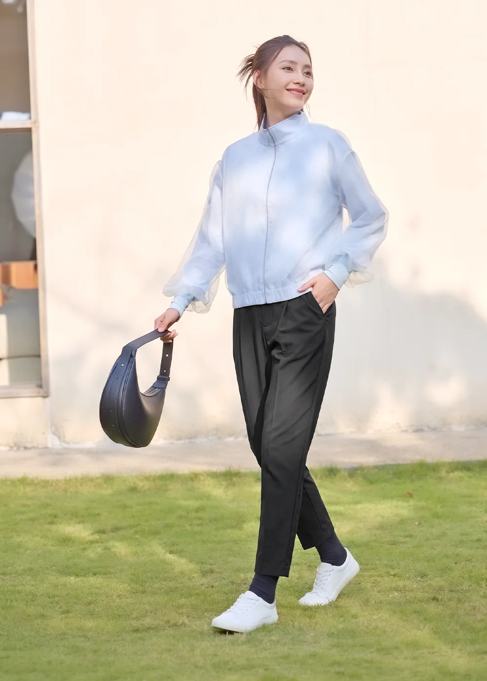 UV100 輕薄透氣防曬外套 OOTD:模特兒身穿淺藍色歐根紗透膚防曬夾克與黑色修飾褲、白布鞋,在戶外草地上展現清爽防曬的休閒姿態。