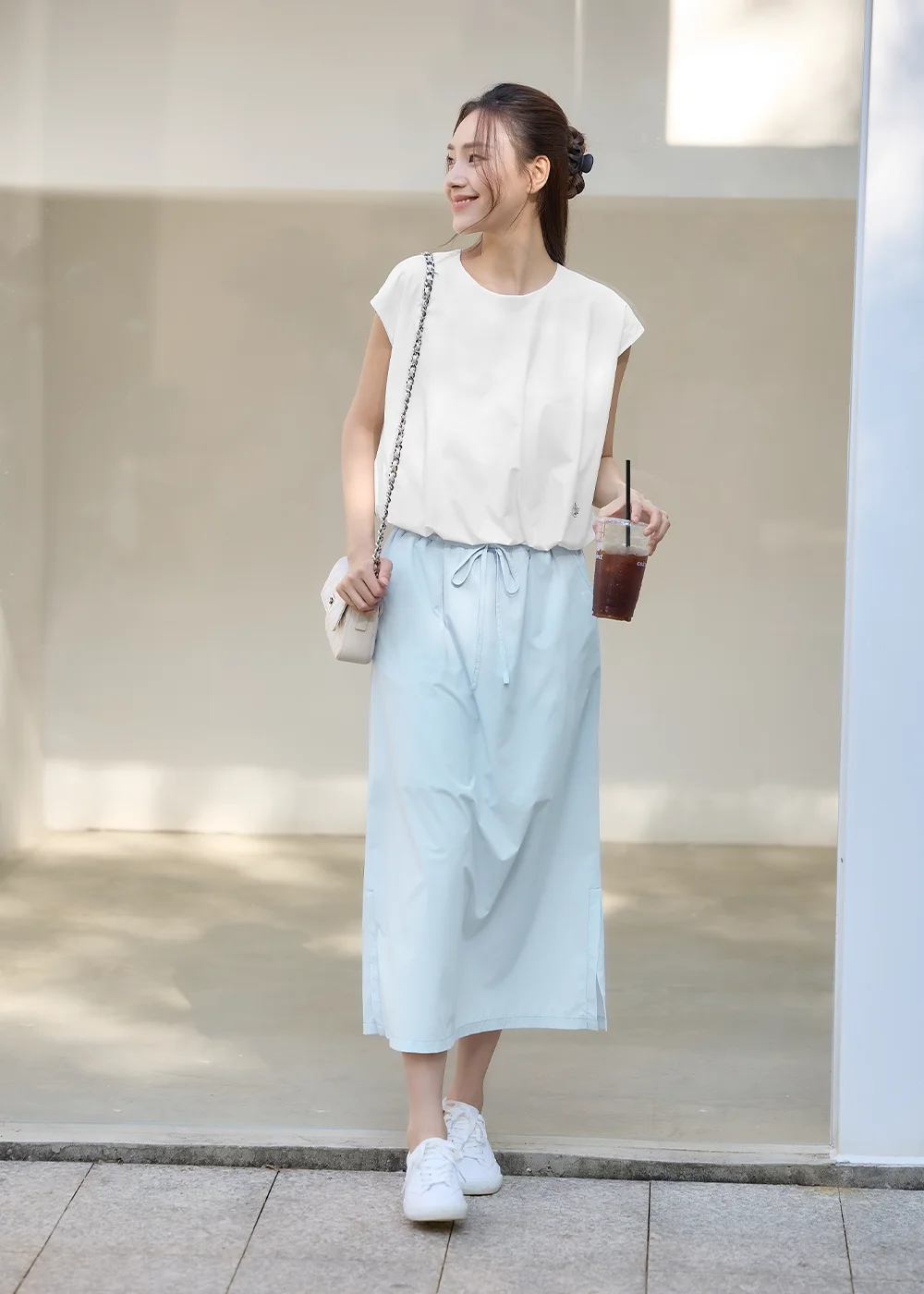 UV100 夏天休閒 OOTD 穿搭:模特兒手拿冰咖啡,身穿白色雲朵蓋袖寬鬆防曬上衣與淺藍色抽繩休閒長裙、白球鞋,呈現清爽舒適的日常生活感。