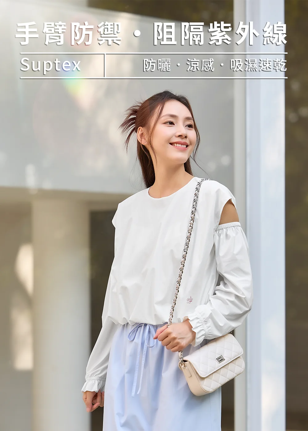 女模特兒身穿白色Suptex機能防曬上衣,採挖肩與浪漫澎袖設計,搭配淺藍色束口褲並肩背白色菱格鏈條包,展現阻隔紫外線與手臂防禦的優雅城市防曬穿搭