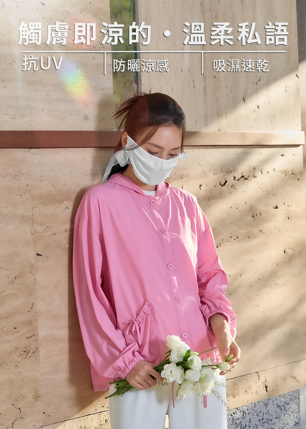 模特兒配戴白色紗帶防曬口罩,身穿粉色機能連帽防曬外套手持白花,背景帶有「觸膚即涼、抗UV、防曬涼感、吸濕速乾」機能標籤文字。