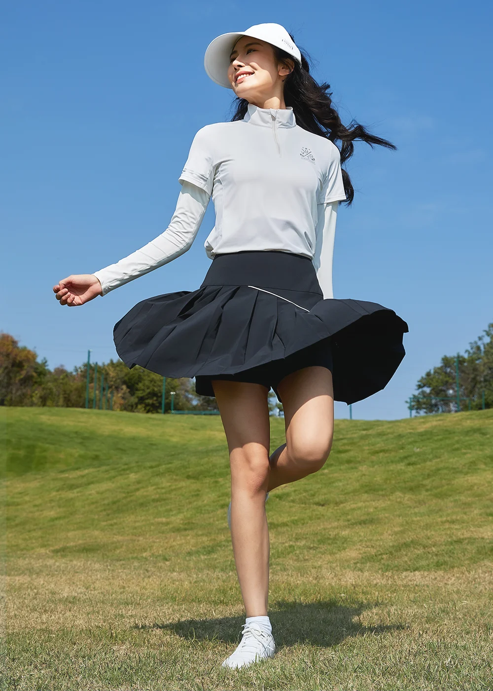 女模特兒身穿Suptex 銀纖維抗菌飄逸百褶短裙炭黑色款，隨風散開的飄逸百褶裙擺，完美顯露內建安全褲的防曝光結構，強調畅快運動不曝光的機能核心。