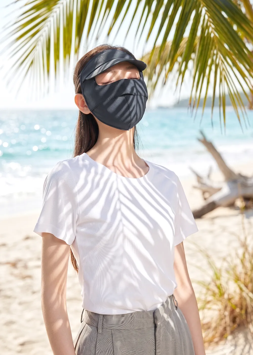 女性配戴機能防曬口罩連遮陽帽，在海灘椰子樹陰影下展示徹底阻隔紫外線的防曬效果
