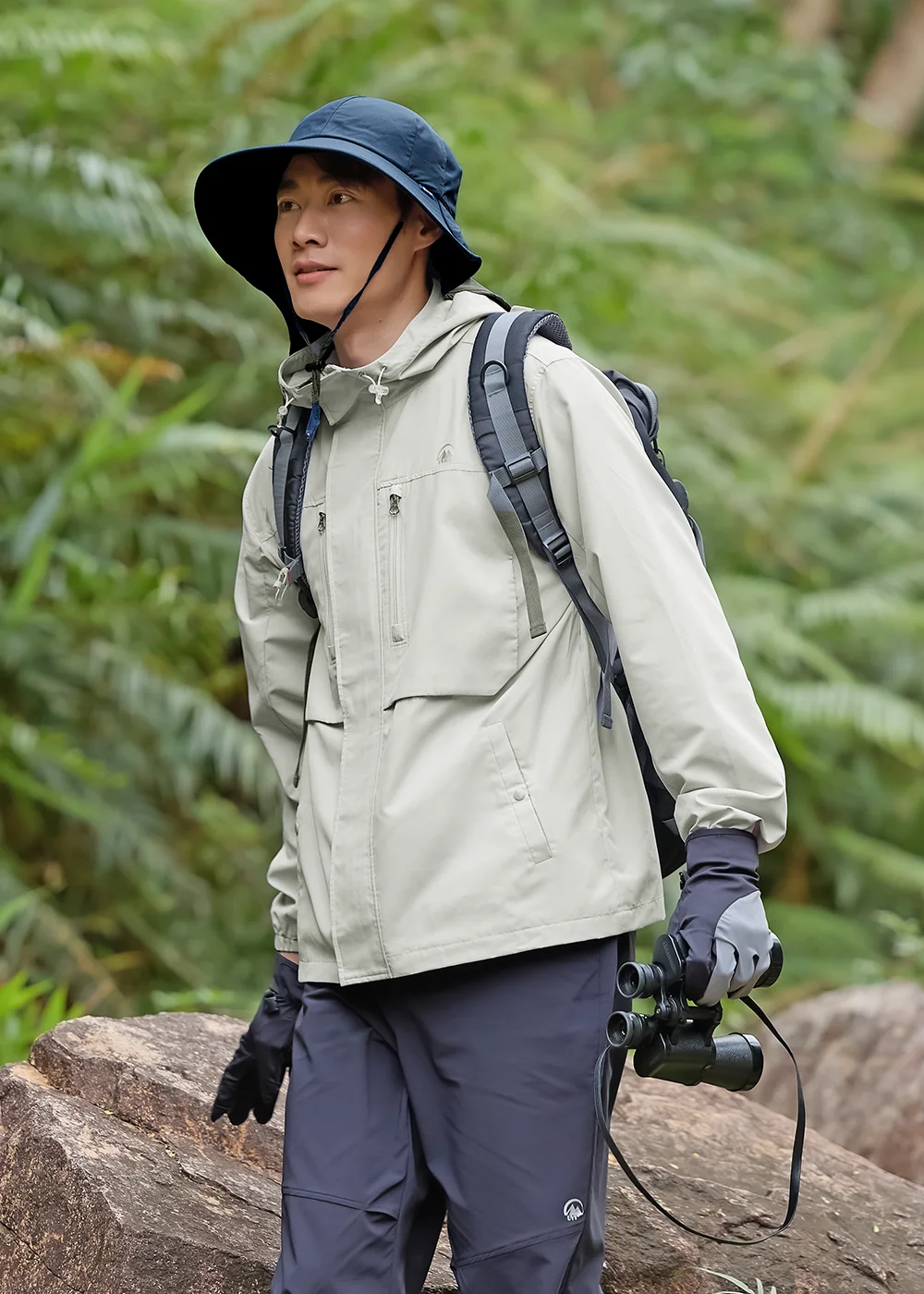 穿著 Suptex 防蚊機能外套與遮陽帽的男模特兒，手持雙筒望遠鏡進行戶外登山健行探索