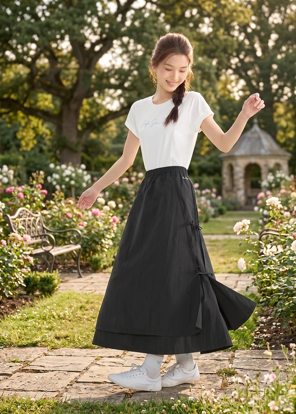 模特兒穿著 UV100 黑色機能長裙在陽光灑落的公園小徑旋轉，展示裙襬的層次剪裁與面料輕盈感，即便穿著長裙也能擁有無限限制的動能。