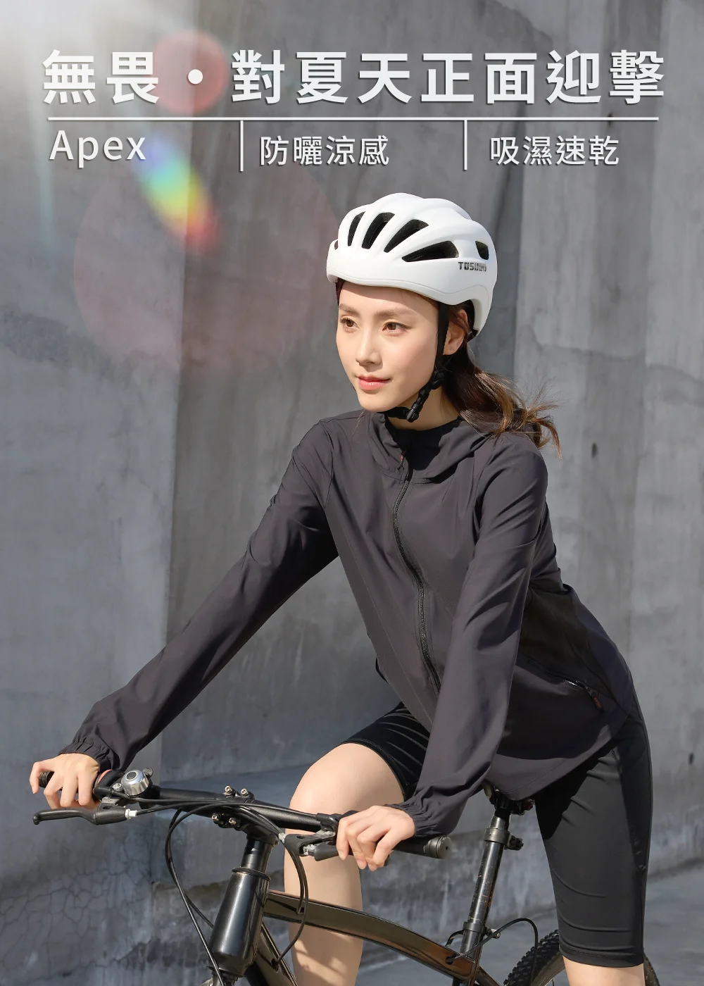 騎單車的女性穿著黑色防曬涼感連帽外套與運動短褲，配戴白色安全帽，背景為灰色水泥牆，上方帶有「無畏・對夏天正面迎擊」與吸濕速乾機能字樣。