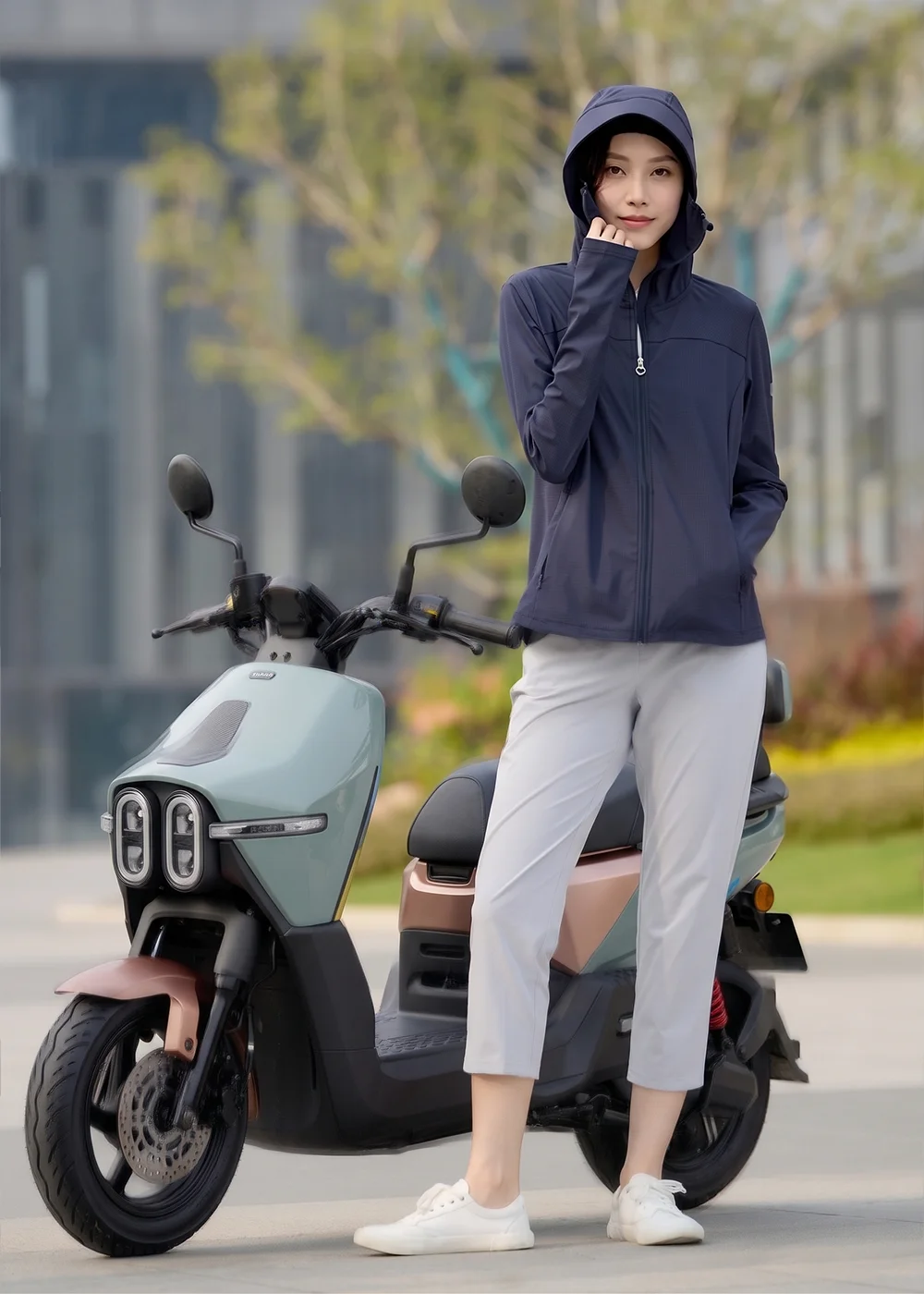 女模特兒穿著 UV100 深藍色 Apex 機能防曬外套與淺灰色長褲，拉鍊拉至領口，展示全方位臉部防護功能