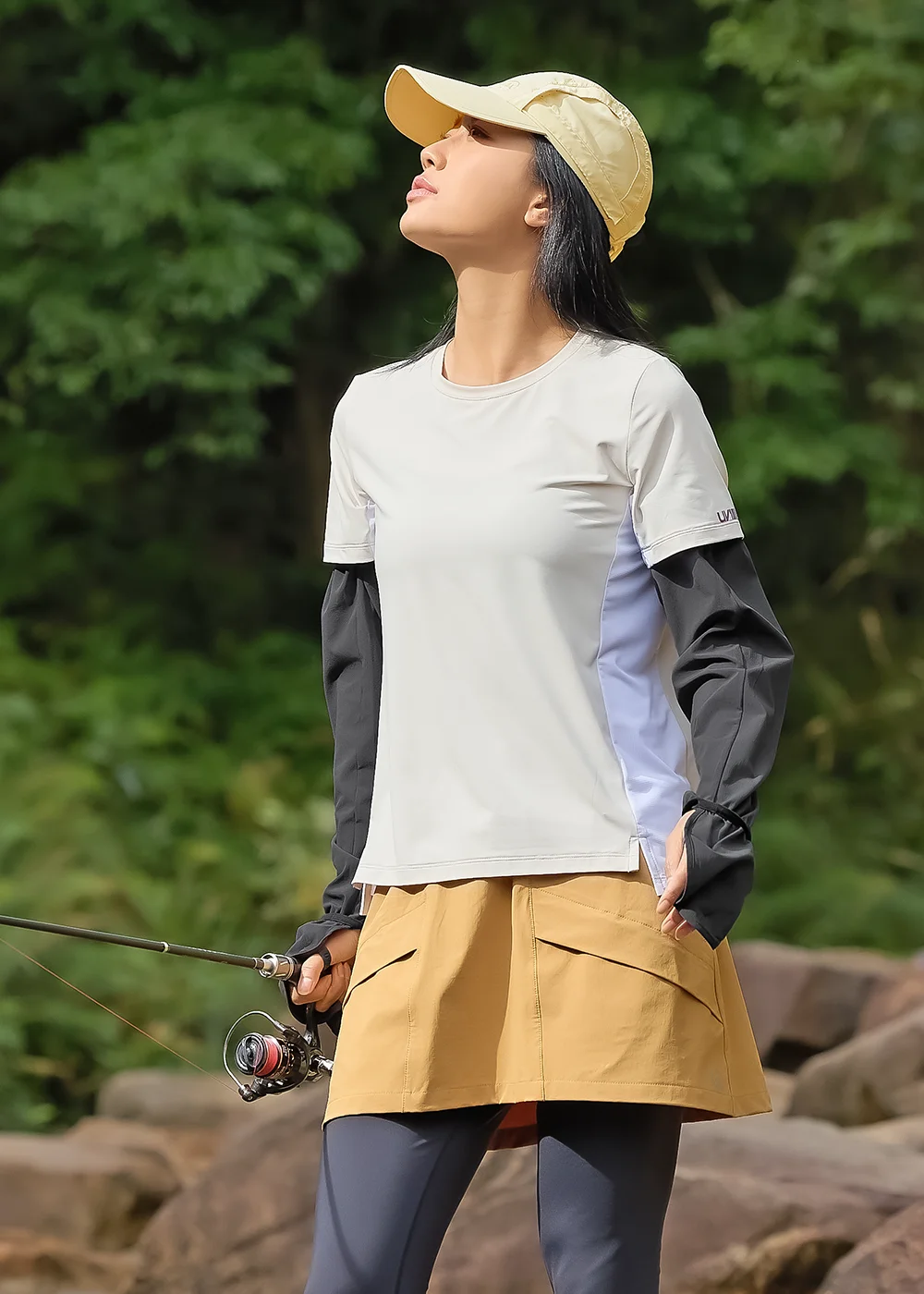 女模特兒穿著 Suptex 防曬袖套於溪邊垂釣，展示產品在強光戶外環境下的實際應用與活動便利性。