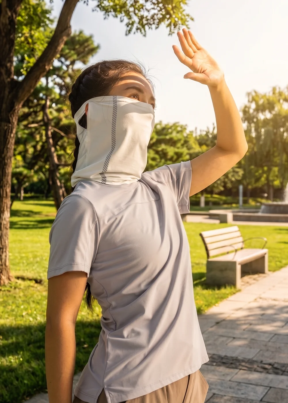女性模特兒在陽光耀眼的公園中，配戴 UV100 白色高效防曬面罩，舉手遮擋陽光，展示面罩在強烈紫外線下的全方位臉部與頸部防曬保護。
