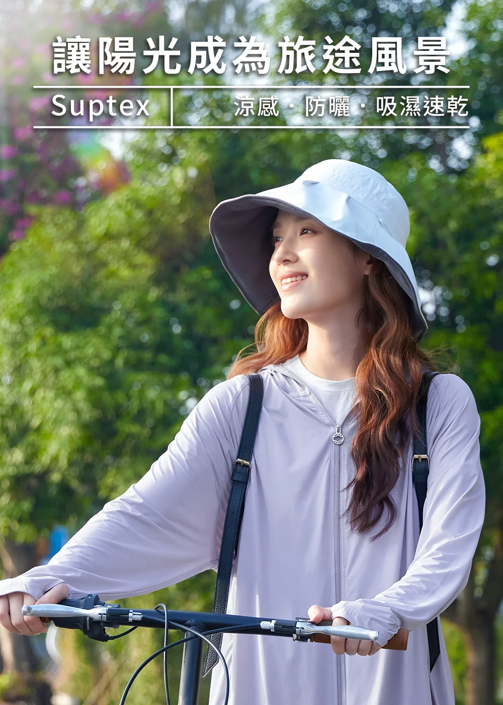 女生戴著UV100女款抗UV寬帽簷雙面遮陽帽，身穿薰衣草紫機能防曬外套在公園林蔭道上享受夏日騎車，提供舒適遮陽與輕量配戴體驗。