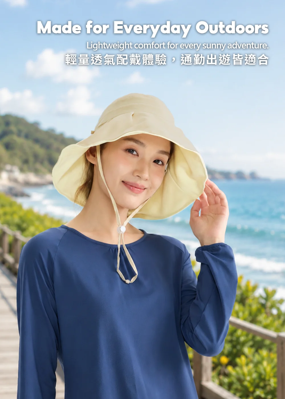 女性戴著米黃色女款寬帽簷雙面防曬帽，身穿深藍色透氣長袖T恤，在蔚藍海岸步道旁享受陽光，示範戶外旅遊渡假防曬穿搭。