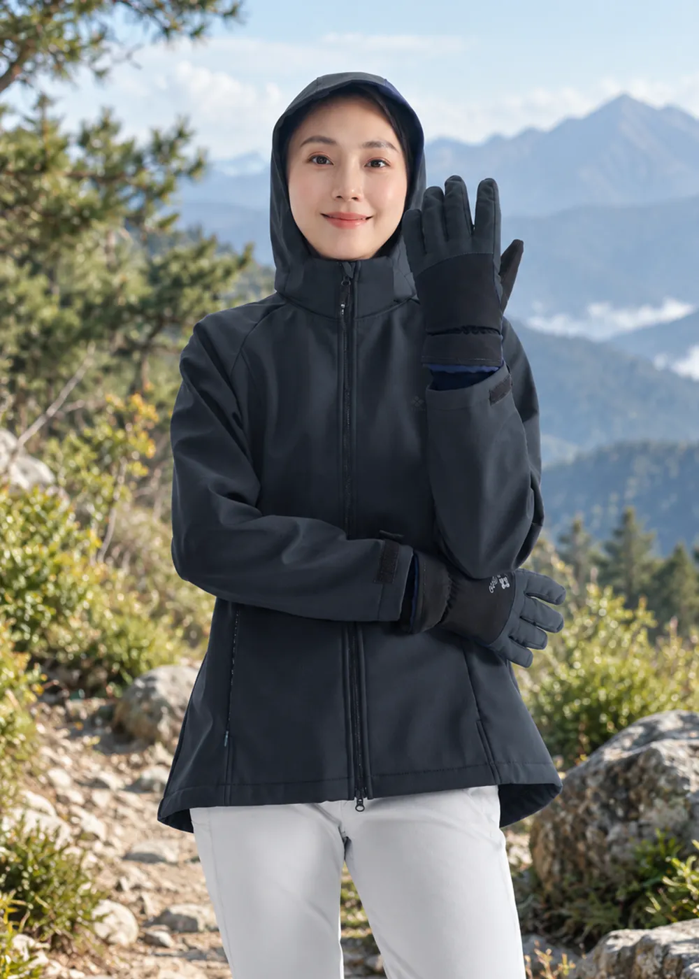女性模特兒戶外穿搭展示：身穿深藍色連帽機能軟殼外套與白色登山長褲，佩戴黑色防風保暖手套，展現手部靈活度與保暖包覆效果。