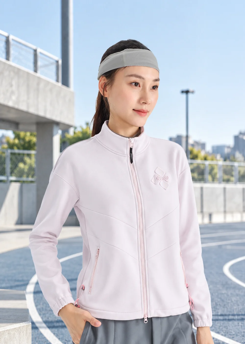 女款運動吸濕排汗灰色髮帶，適合跑步、健身時固定頭髮與吸汗。模特兒穿著淡粉色運動外套與灰色短褲，於戶外藍色跑道上展示。機能布料舒適彈性，保持臉部乾爽。