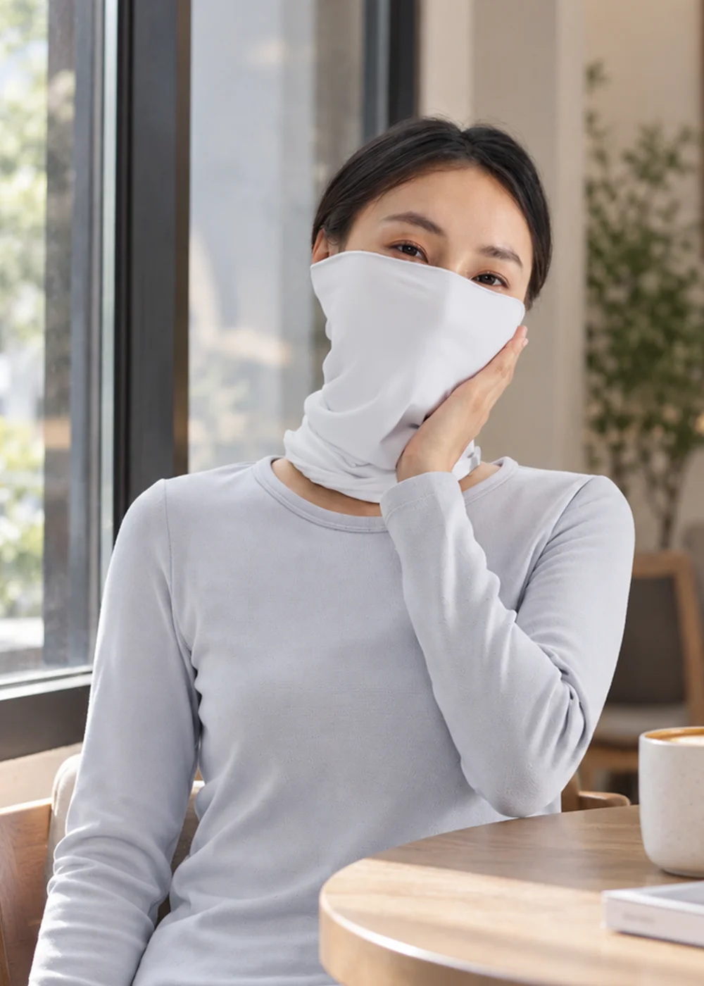 女性戶外保暖白色頸巾、面罩。模特兒於咖啡廳室內展示頭巾多用途，可作為圍巾、蒙面、頭帶使用。機能布料親膚柔軟、透氣舒適，適合冬季戶外與旅行穿搭。